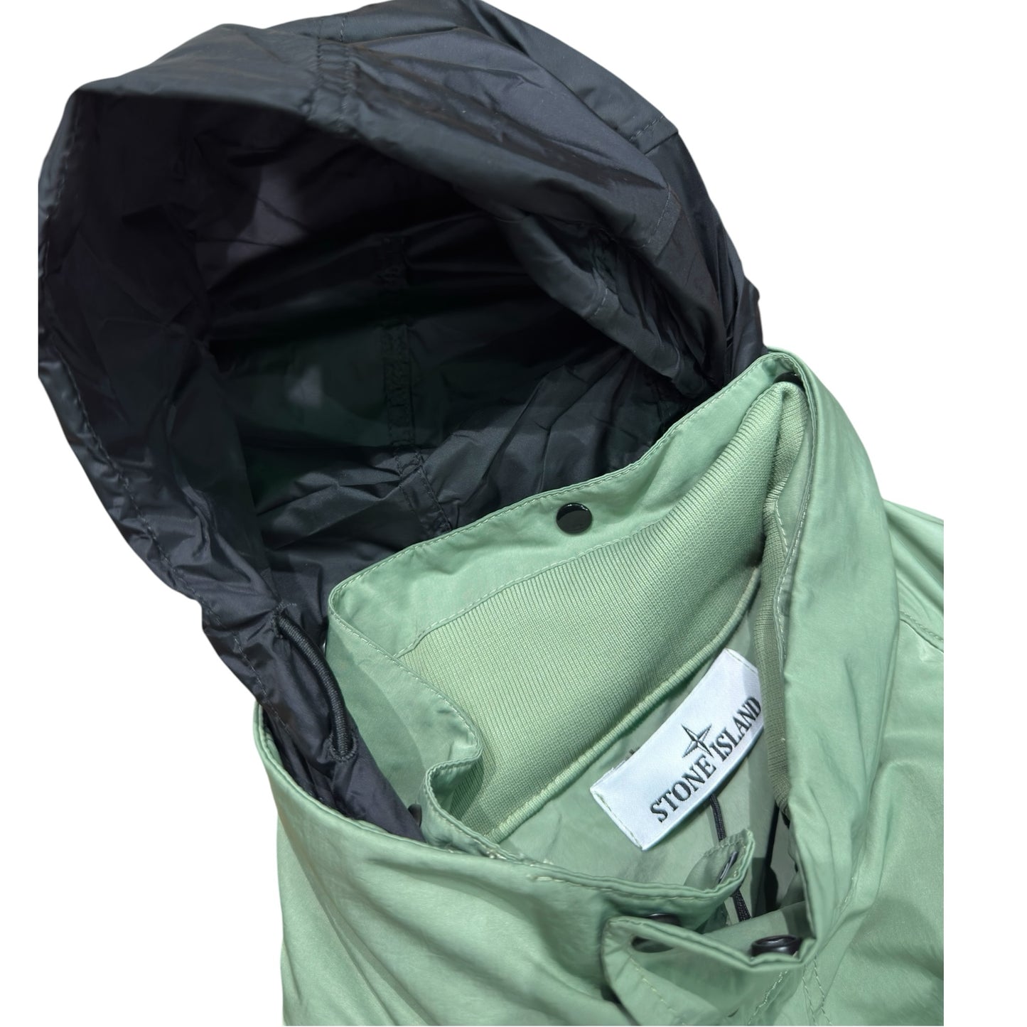 Urban Saints Stone Island sage green field jacket featuring a contrasting black hood and internal brand label detail.
