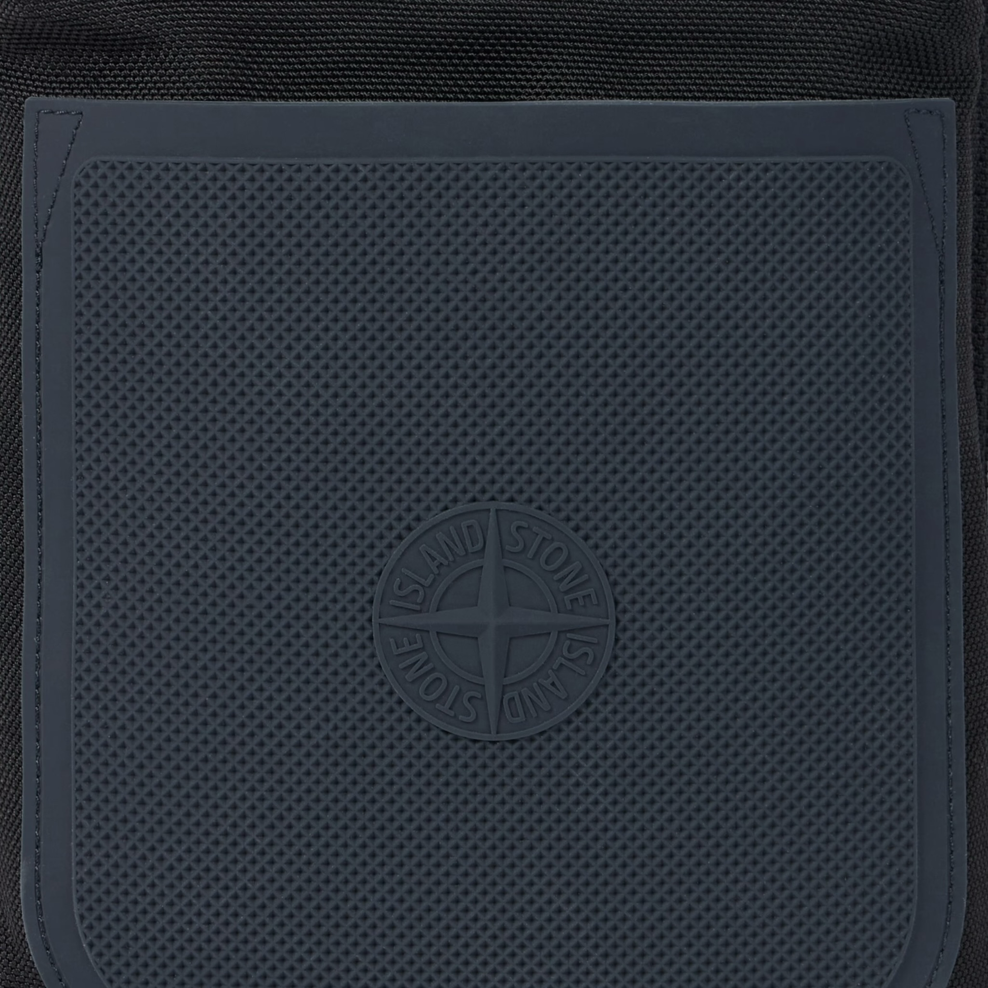 Urban Saints Stone Island black nylon crossbody bag with navy blue textured rubber panel and embossed logo.