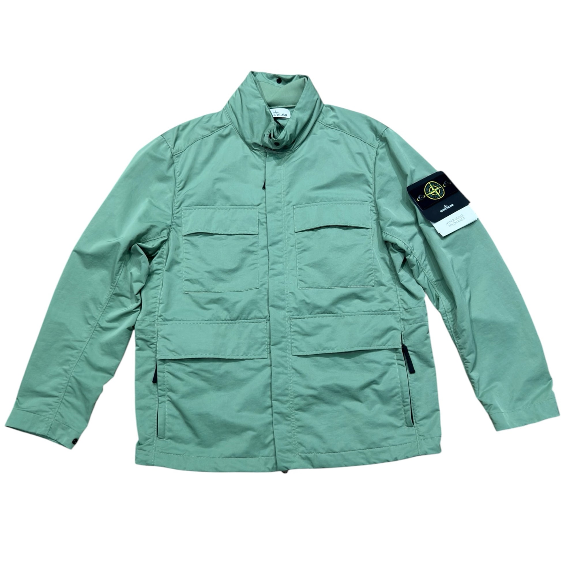 Urban Saints Stone Island sage green field jacket with utility pockets, high collar, and iconic sleeve logo patch.
