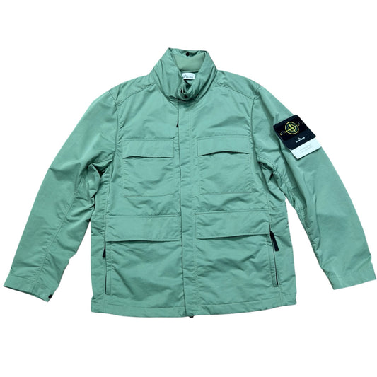 Urban Saints Stone Island sage green field jacket with utility pockets, high collar, and iconic sleeve logo patch.
